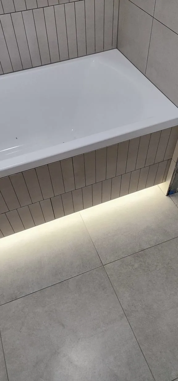 Ванная с вертикальной плиткой и тёплой LED-подсветкой под экраном ванны